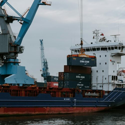 A cargo ship loaded with shipping containers at an industrial harbor with cranes.